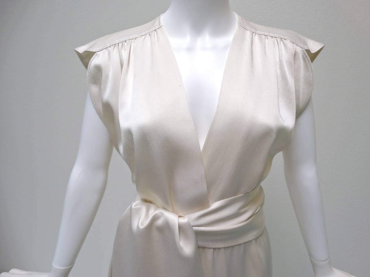 This is a beautiful Silk Saint Laurent for Yves Saint Laurent circa 1970's off white gown with a v-neck neckline and a detachable sash belt. This dress has a beautiful cut, great cap sleeves and a slight train on the back bottom hem. Marked size 40.