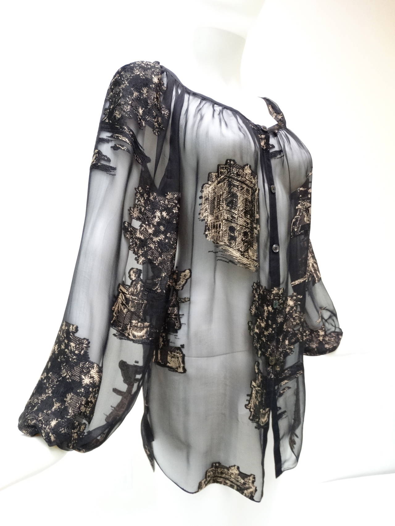This rare beautiful sheer Hermes blouse is made from light as air, sheer jet black silk with a tan and black French scenic prints in silk. It has a very loose fit, buttons up the front with a scoop neckline and has big billowy sleeves. All buttons