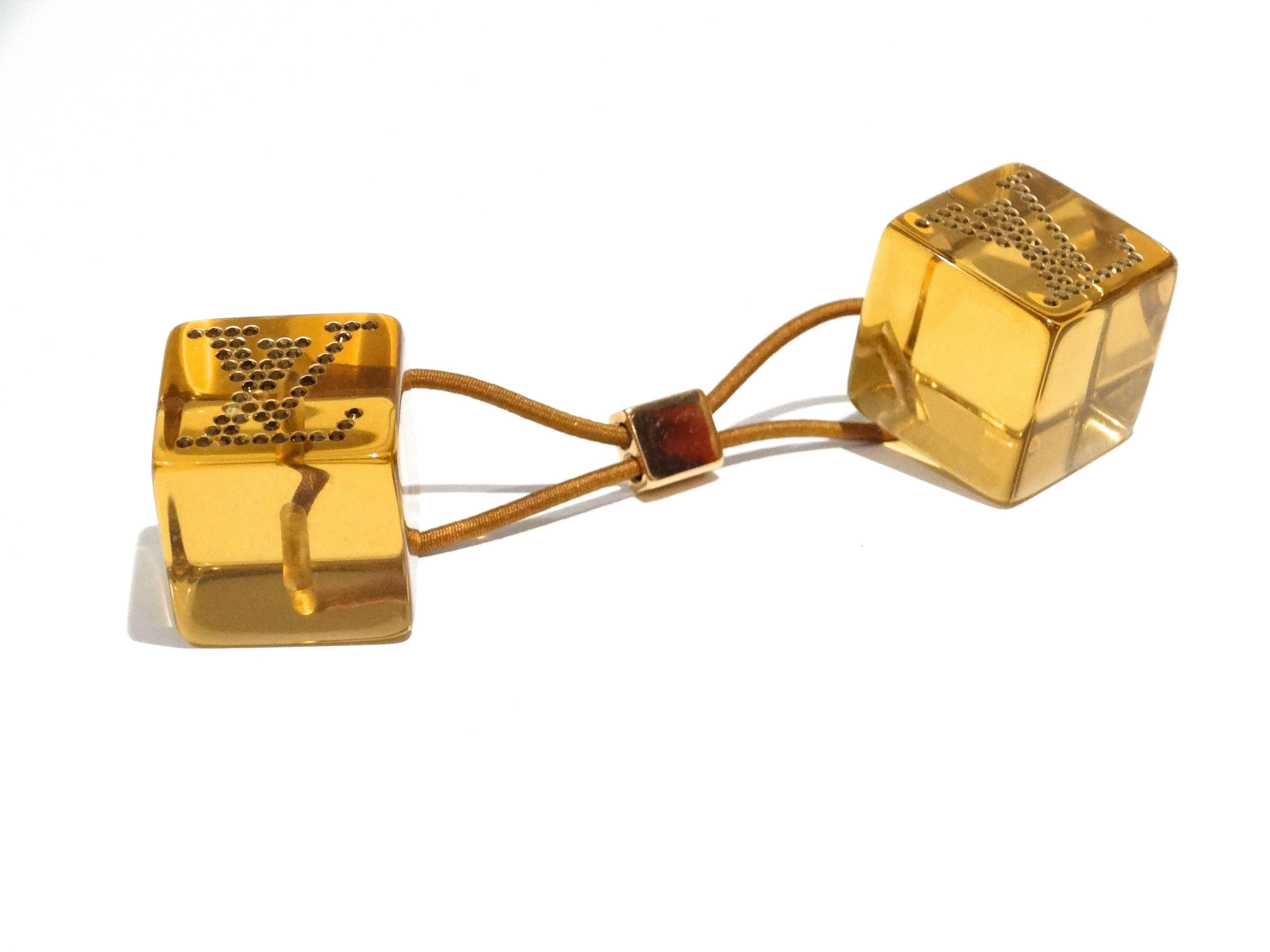 Bringen Sie etwas Spaß in Ihr Haar mit diesem bezaubernden Louis Vuitton Amber Resin Hair Cube! Sie bestehen aus farbigem und klarem Harz mit dem Louis Vuitton Logo in Kristallen auf jedem Würfel und sind ein perfektes:: einzigartiges