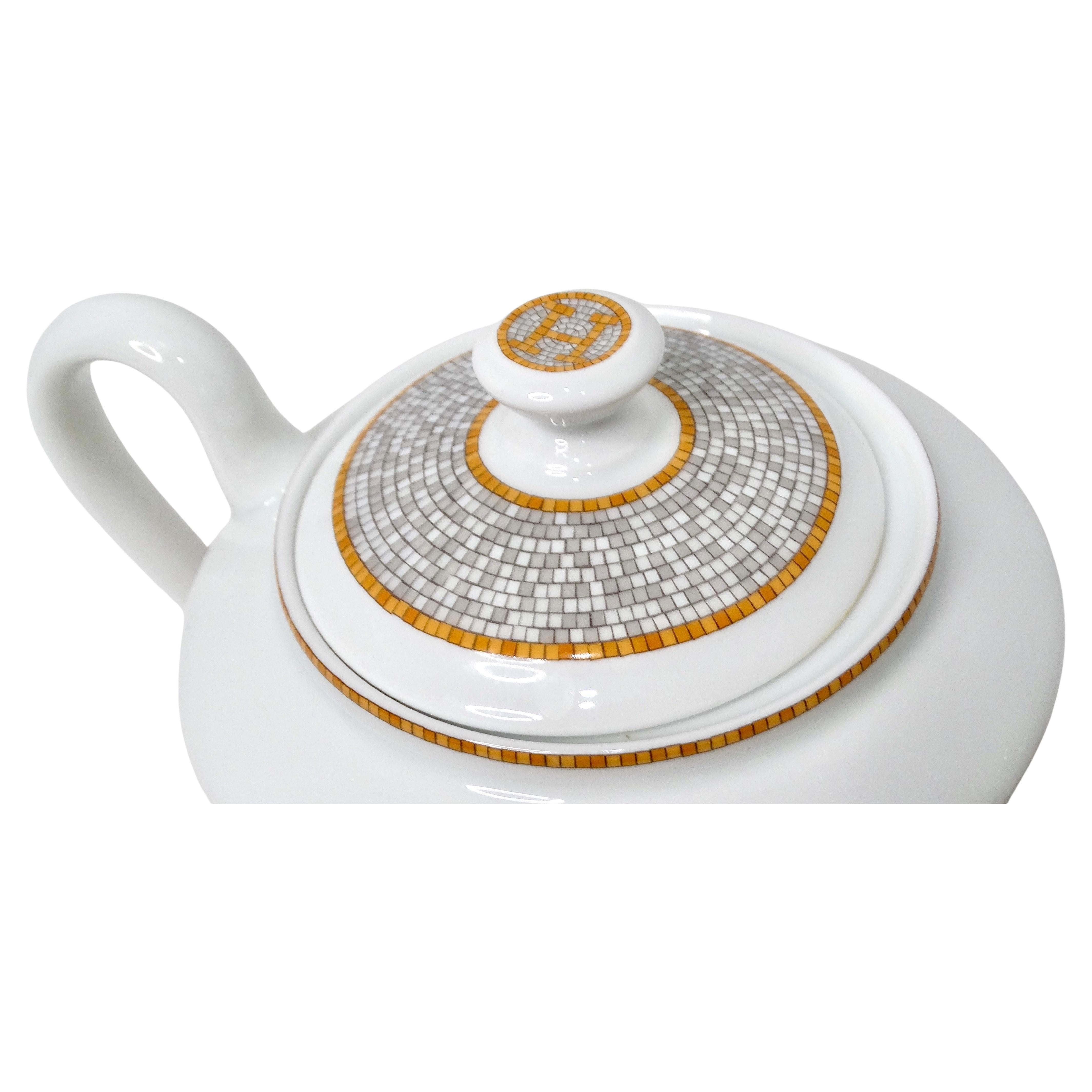 La teiera in porcellana Hermes Mosaique au 24 Van Quatre Gold è uno straordinario esempio di artigianato di lusso e design artistico. Caratterizzata da una vivace stampa a mosaico nei toni del giallo, dell'arancio, del bianco e dell'oro, questa