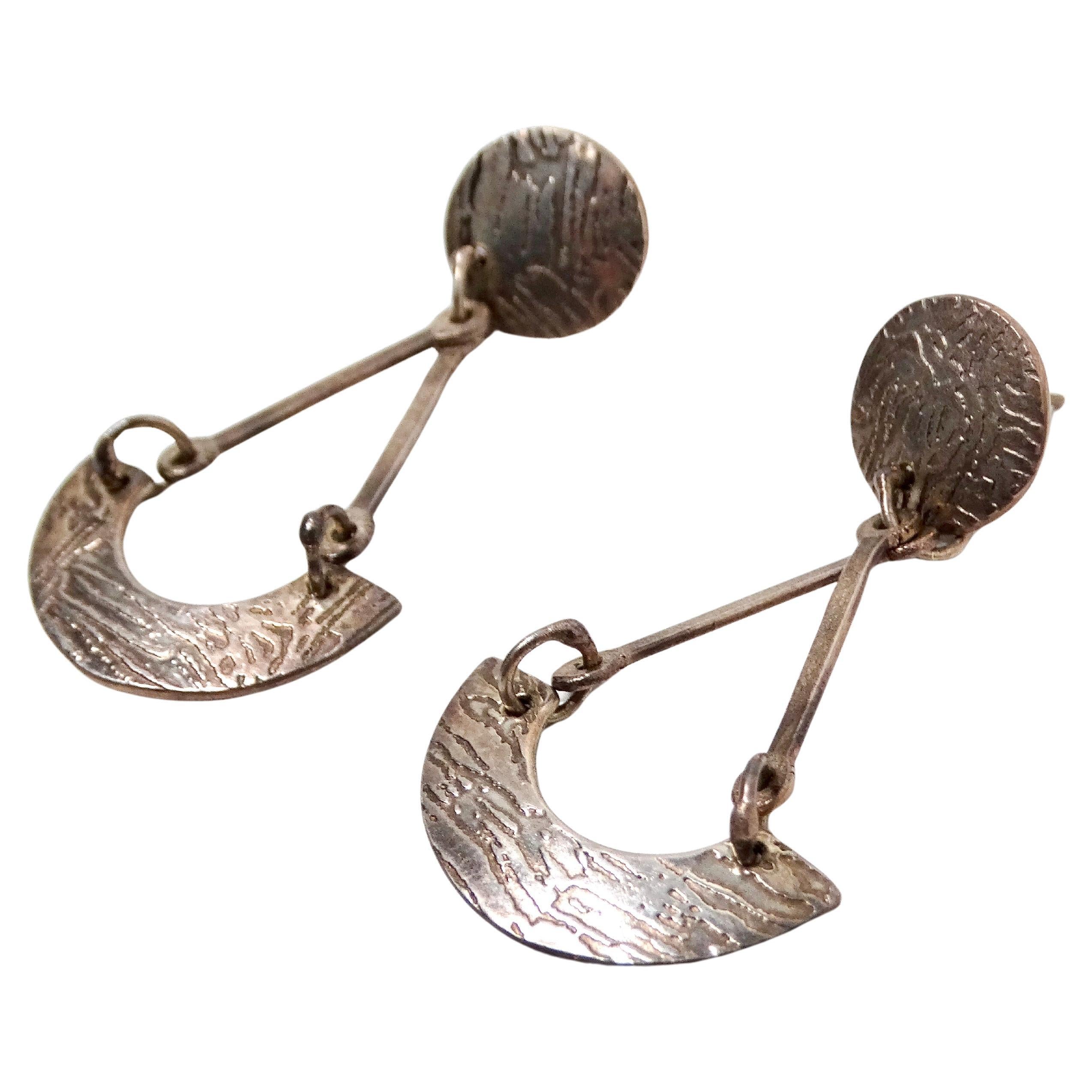 Gli orecchini a penzoloni geometrici in argento sterling testurizzato sono uno splendido esempio di design di gioielli contemporanei, che fondono forme geometriche moderne con l'artigianato. Realizzati in argento sterling, questi orecchini