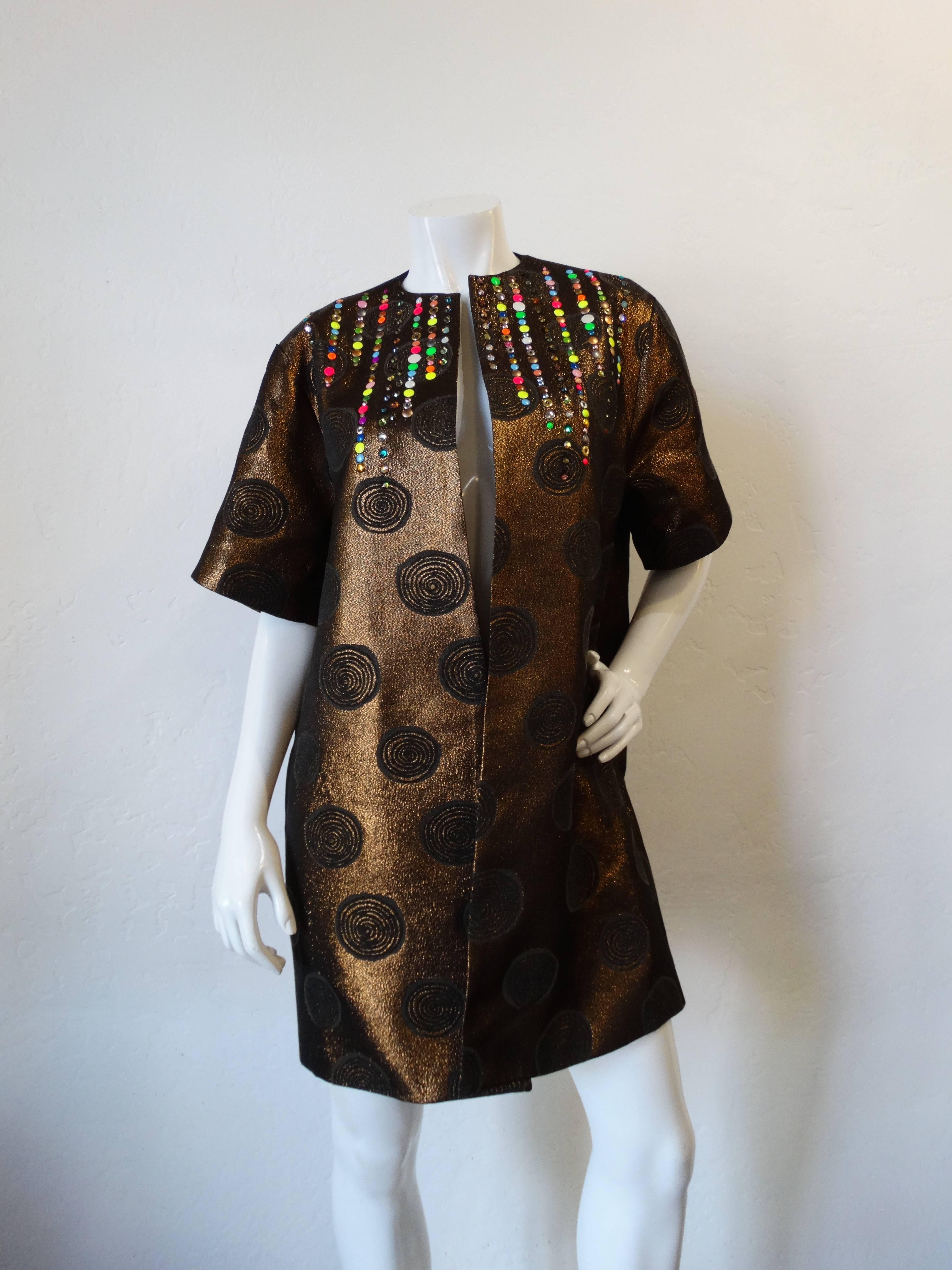 Incredible piece from the well-sought after brand Libertine! Metallic woven fabric embroidered with swirly dots and accented with rainbow studs around the collar. Short sleeves with a swing-coat like fit. Pockets at either side. Black satin lined