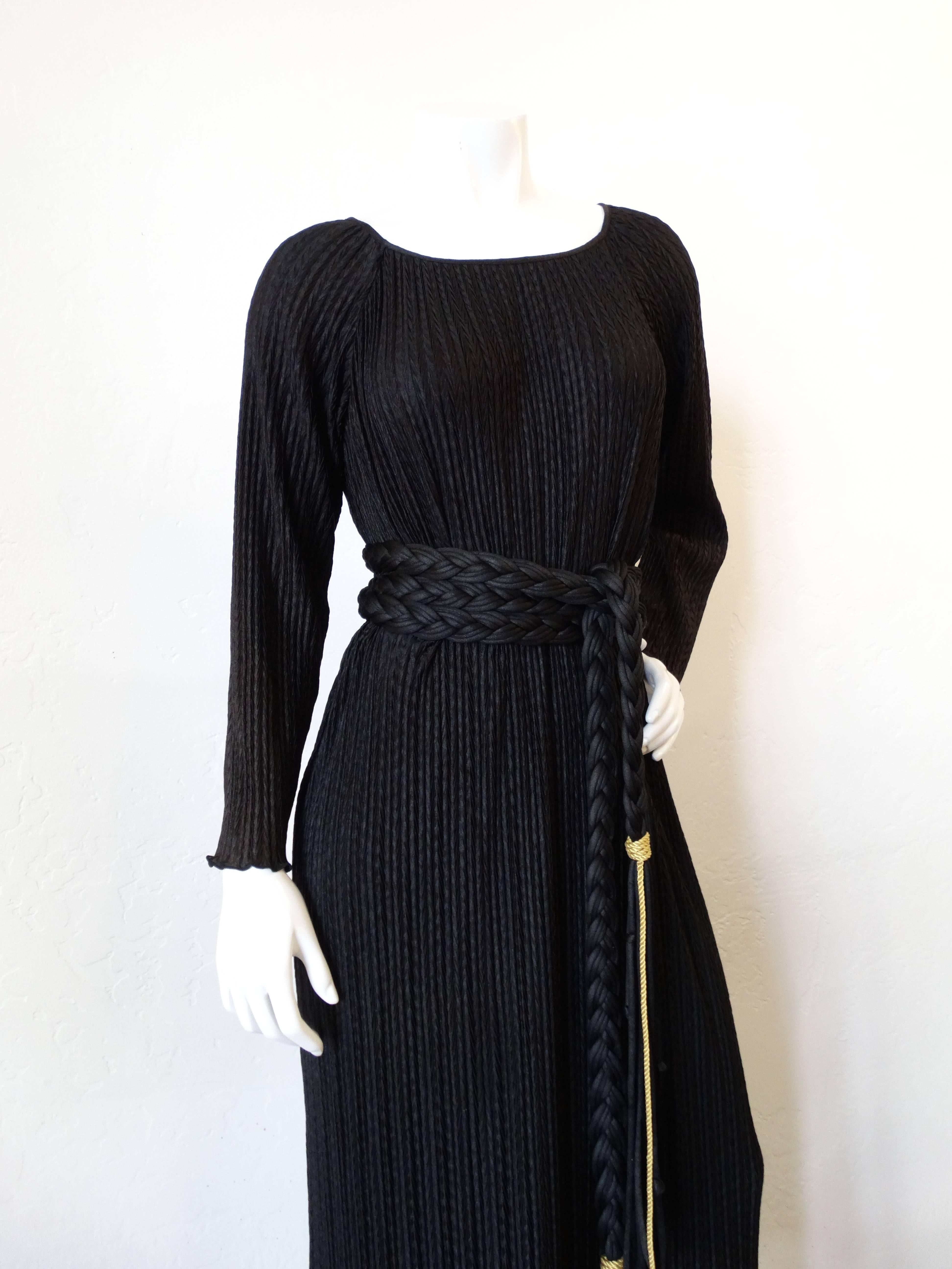Incredible 1970s gown from designer Mary McFadden! Made out of soft and silky black fabric with Fortuny pleating. Grecian style with incredible wrap around braided belt- accented with gold cord. Non-fitted tunic style, tiered bottom accented with