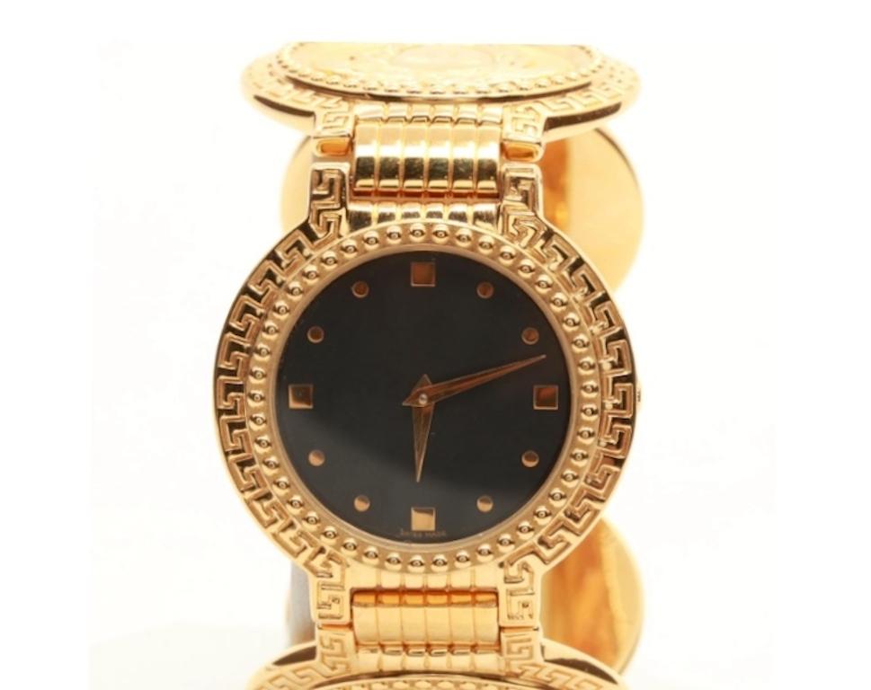 A Gianni Versace gold plated stainless steel wristwatch. This watch features a stainless steel back with a gold plated bezel housing a black dial with gold-tone hands and indexes. The bracelet is composed of gold plated circular discs containing the