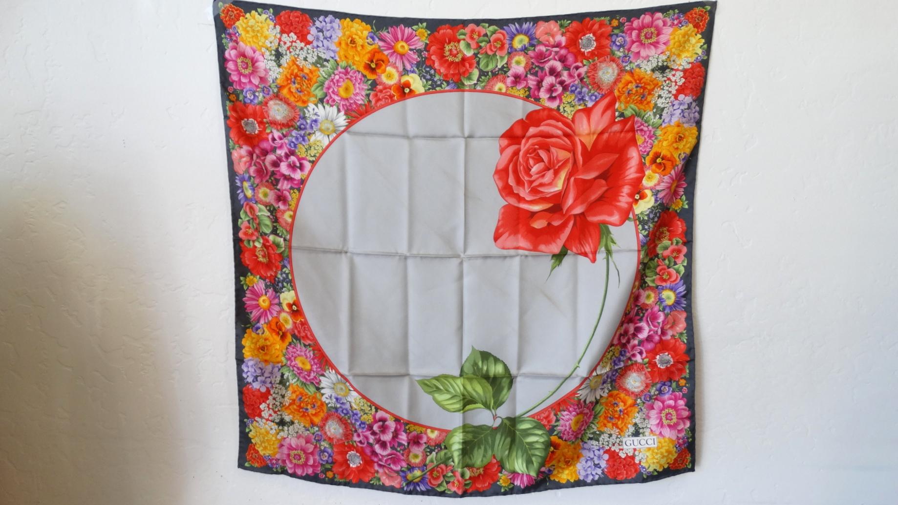 Gorgeous, Vibrant and Gucci, What More Could You Ask For In A Scarf!? Circa 1980s, this Gucci scarf features a dark pearly grey trim and a colorful floral motif boarder with a silver circle in the center, accented with a large blooming rose. 