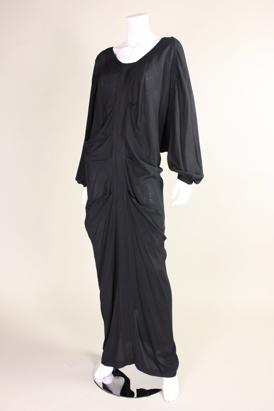 Yohji Yamamoto black gown is made of 100% rayon fabric and features pleated details at the center front.  Open back ties at the center back.  Dolman sleeve with elasticized cuff.  Center back exposed metal zipper.  Three pockets. 