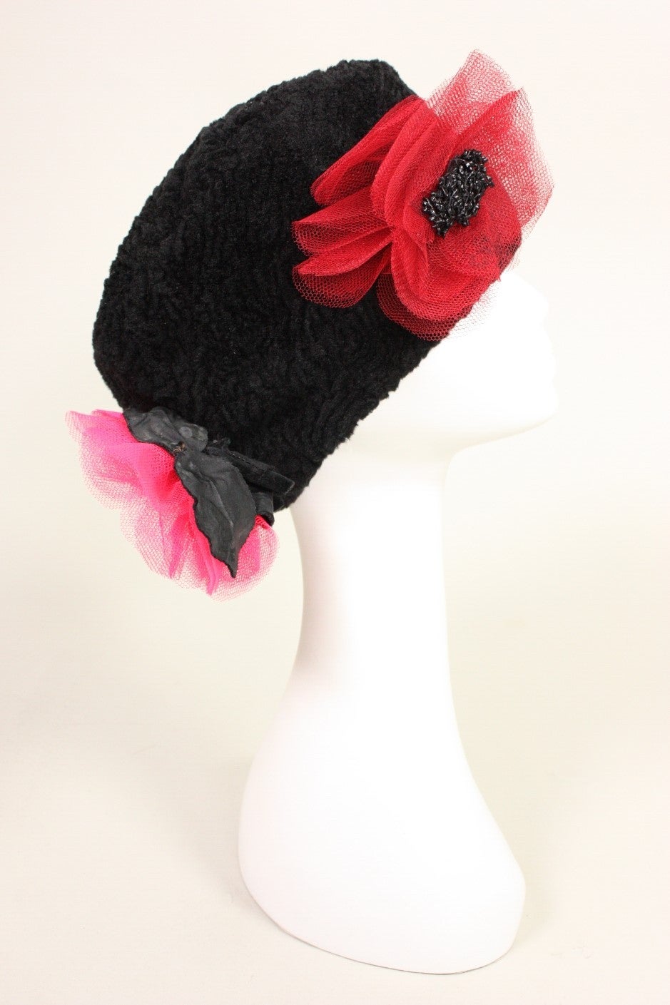 Vintage hat from Yves Saint Laurent is made of black fabric that resembles broadtail. It features four large net flowers and black velvet leaves. Lined.  Interior circumference measures 20 1/4