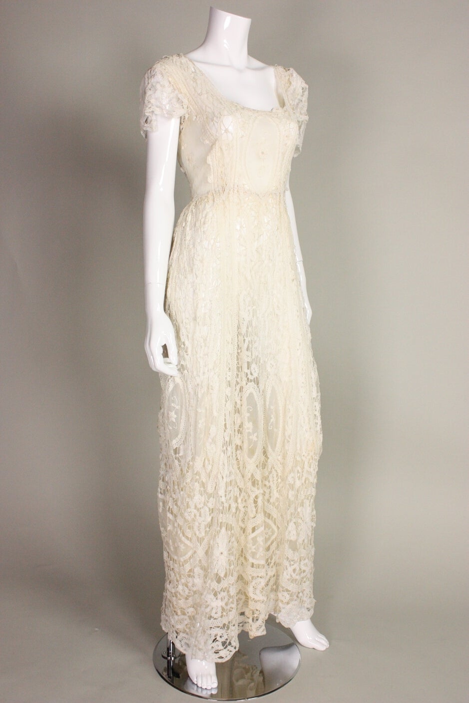 Beautiful gown dates to the Edwardian era and is made of ivory Battenburg lace.  Squared scoop neckline.  Lace is gathered at center lower back, just above the buttocks.  Short sleeves. Lined with a very fine silk. Closes in back with a series of