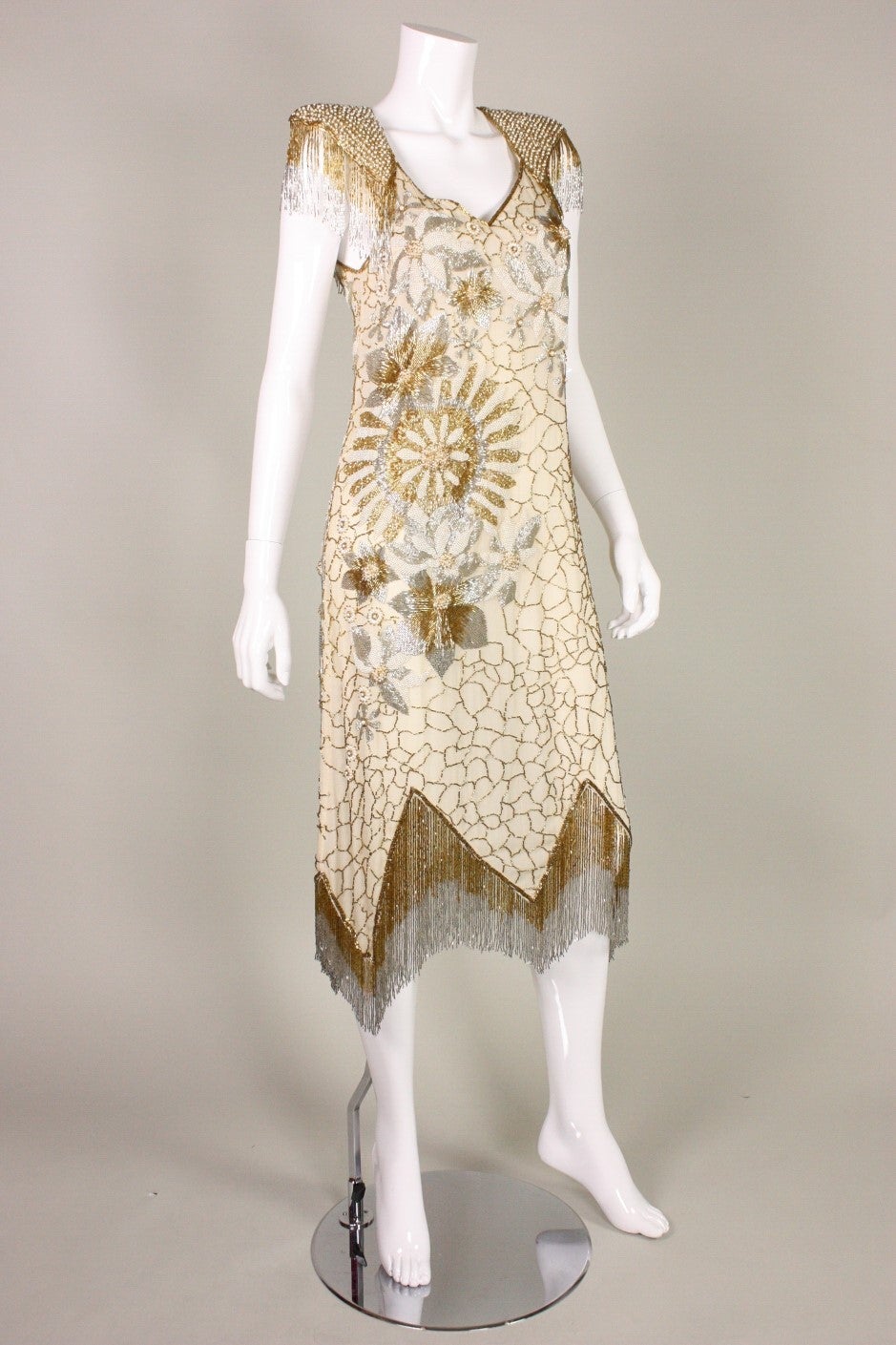 Vintage dress from Los Angeles-based designer Birgitta dates to the 1980's and is made of cream silk chiffon.  It was completely beaded by hand using gold, silver, and pearlized beads.  Beaded fringe at padded shoulders and zigzagged hem.  Center