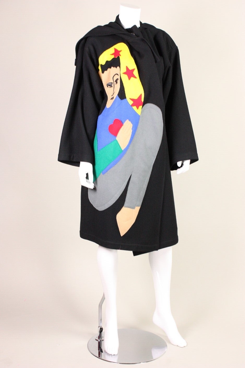 Lovely coat from Jean-Charles de Castelbajac for Ko & Co. retailed at Neiman Marcus and was made of black wool.  A brightly colored figure is appliqued on the right side. D-ring closures on both sides of neck are fastened to narrow wool strips. 