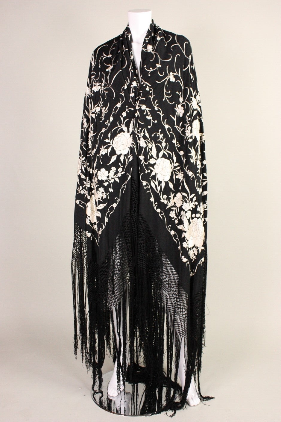 Gorgeous piano shawl dates to the 1920's. It is made out of black silk with cream-colored hand-embroidery throughout. Fringed and macrame edges.

Measurements (of embroidered silk only): 60