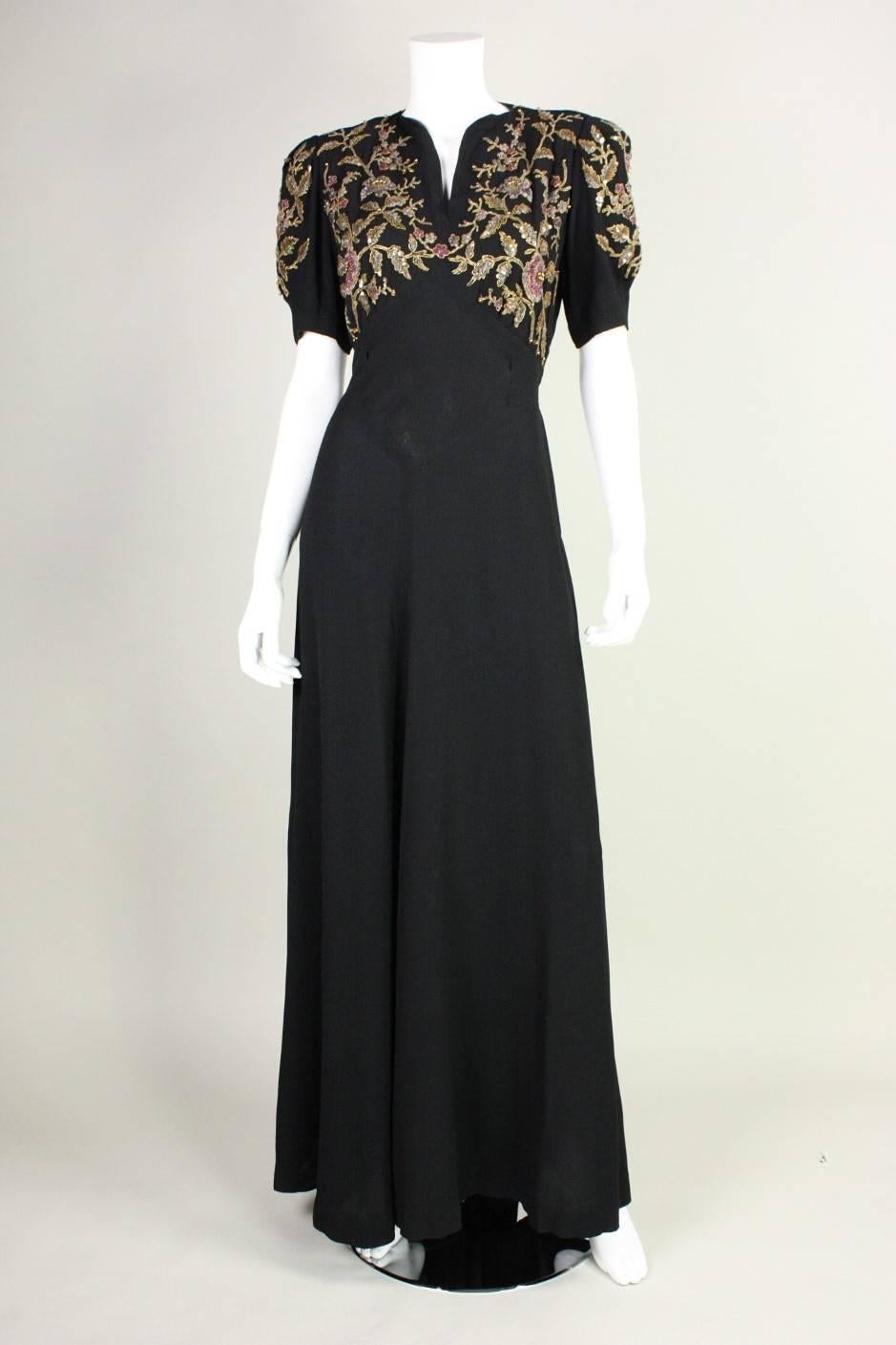 Vintage black crepe gown dates to the 1940's and has fabulous floral ornamentation on bust and sleeves.  Ornamentation includes pastel seed beads, larger brass-colored spherical bead highlights, and raised gold outlines. Bodice features v-neck and