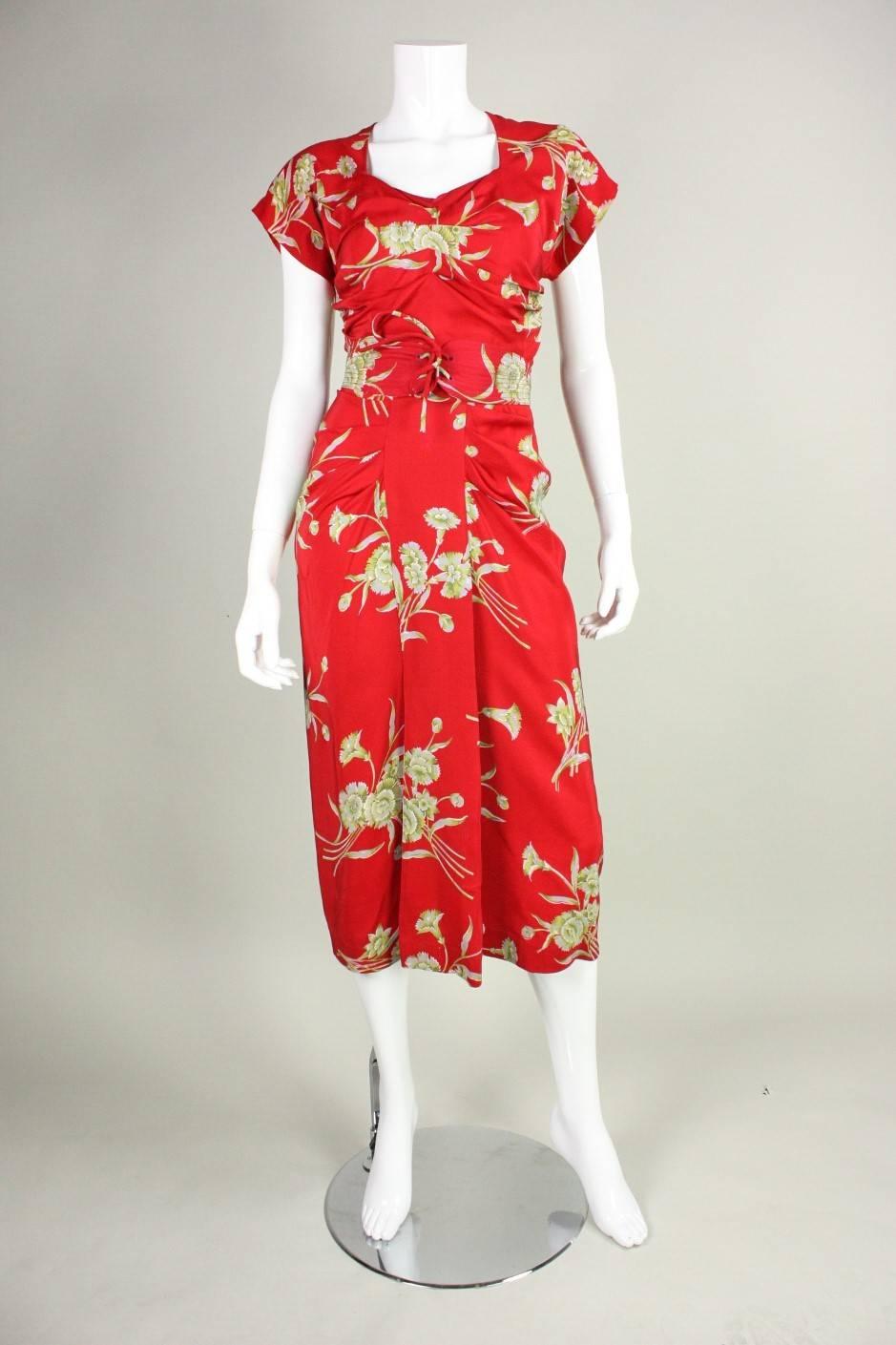 Vintage dress dates to the 1940's and is made of red silk with an allover floral print.  Center front bodice and hip feature wonderful ruched detailing.  Detached belt has concentric stitching and laces at the center front.  Mostly unlined.  Side