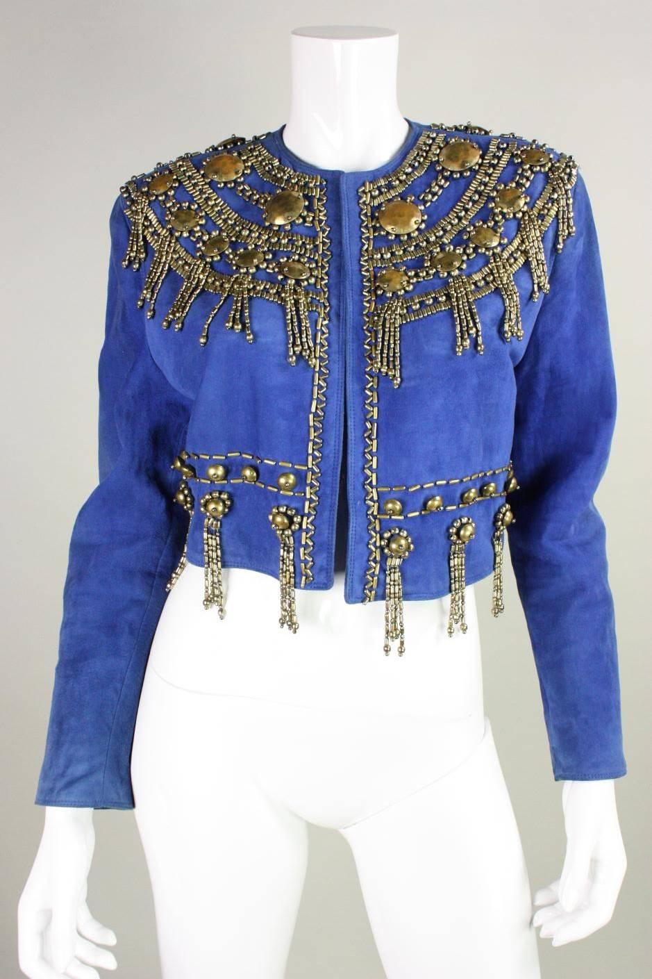 Gorgeous jacket from Gianni Versace dates to the early 1990's and is made of royal blue suede.  It features brass-toned ornamentation in various sizes and shapes arranged in a concentric pattern around the neck and around the waist.  No closures. 