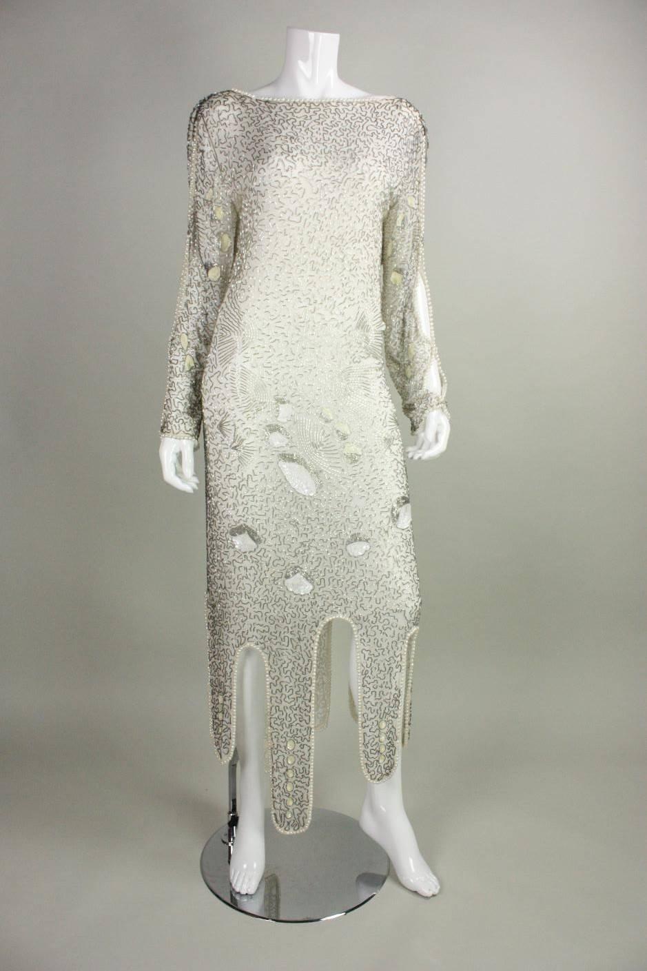 Vintage cocktail dress dates to the 1980's and is made of white silk that is adorned throughout with silver-colored bugle beads, white sequins, and faux pearls.  Long sleeves have openings down the outer sides that are lined with pearls.  Boat neck