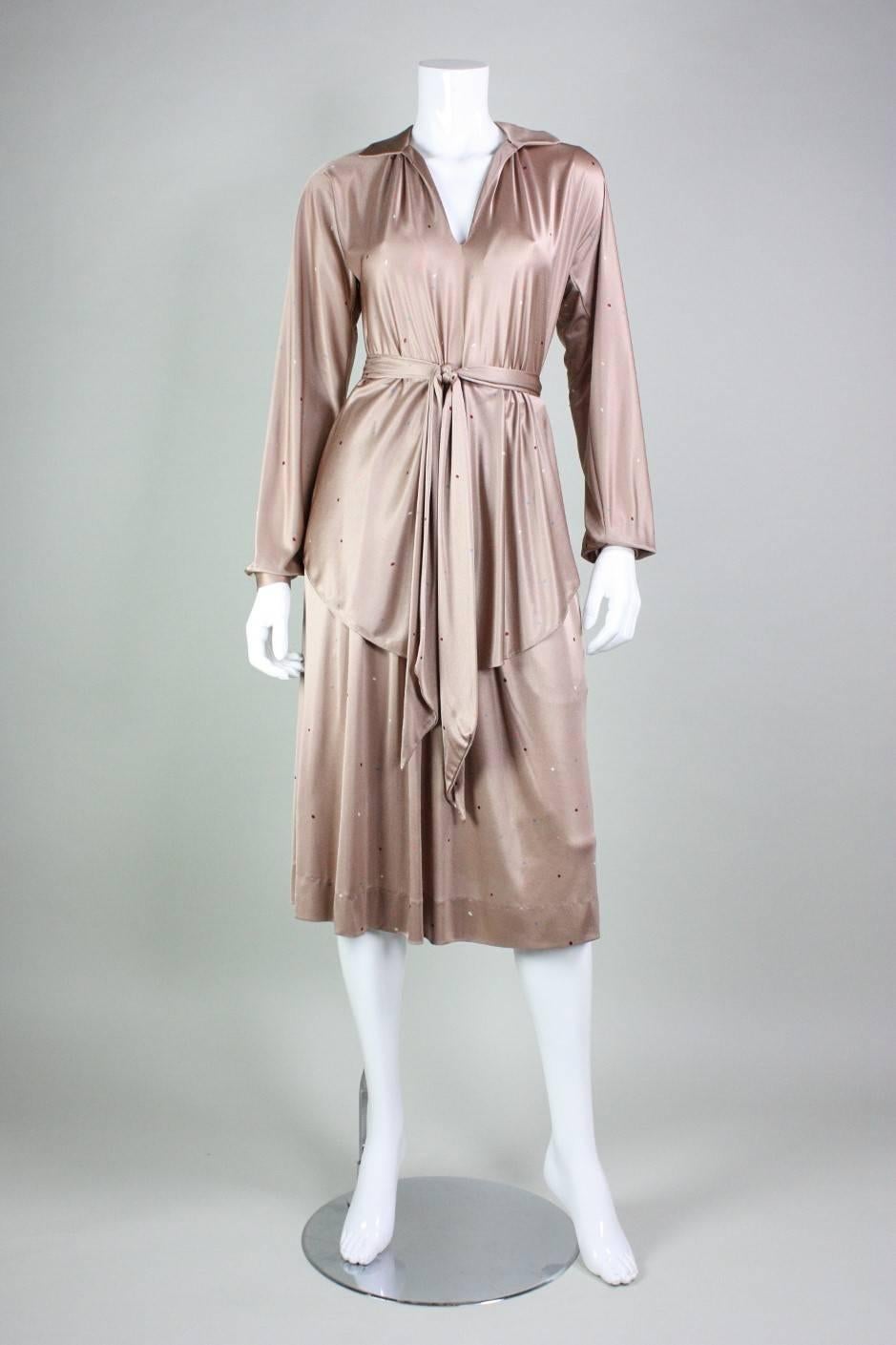 Vintage ensemble dates to the 1970's and was manufactured by Halston IV.  It is made of a super soft and liquid-like tan polyester jersey with a dot print.  Tunic blouse has a v-neck, turn down collar, and snap cuffs.  Below knee-length skirt has a