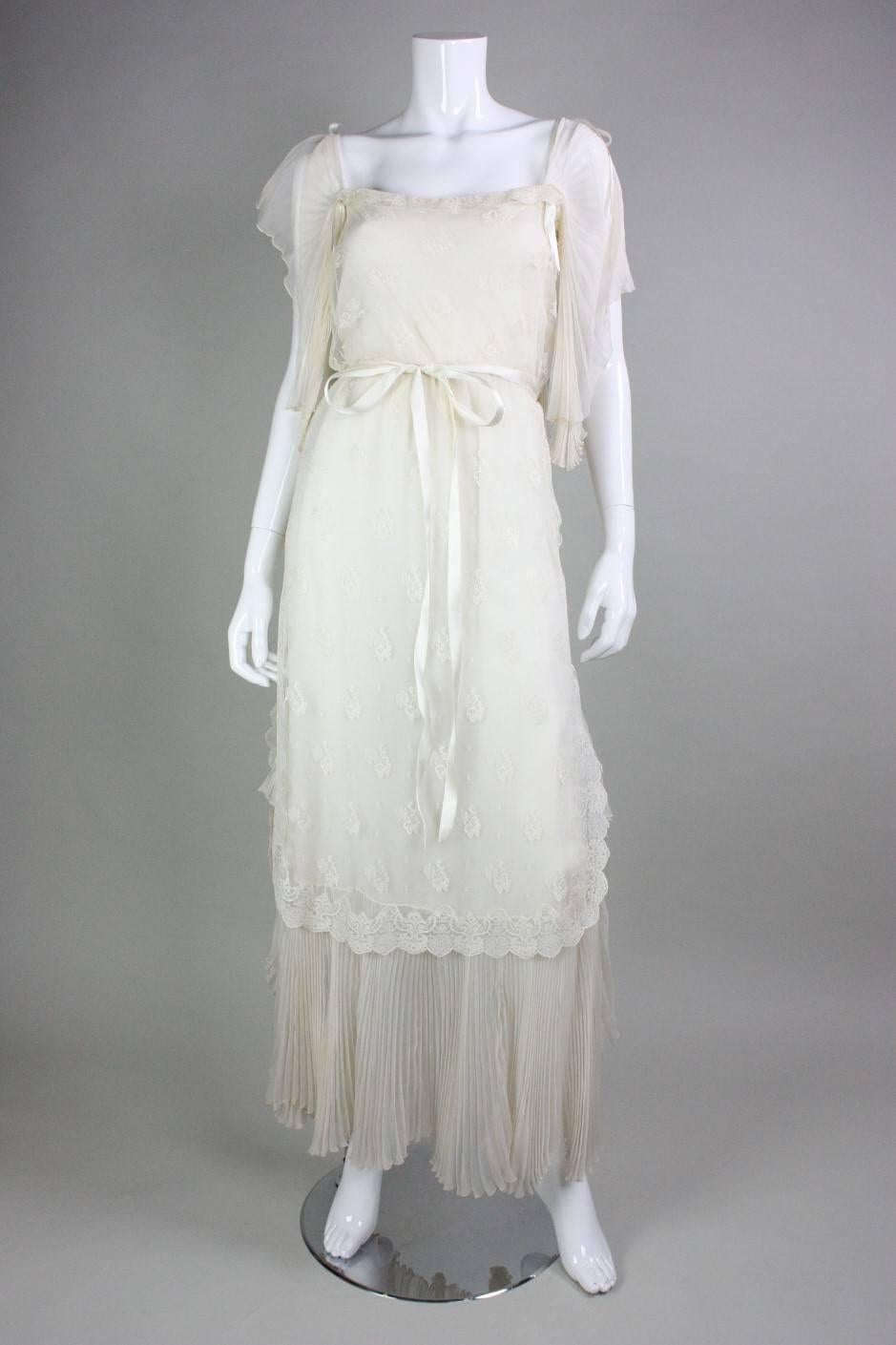Ethereal gown from Tan Giudicelli dates to the early to mid-1980's.  It is made of silk chiffon that is layered with cream-colored lace.  Pleated sleeves and hem.  Ribbon detailing and detached ribbon belt.  Side snap and hook and eye closure. 