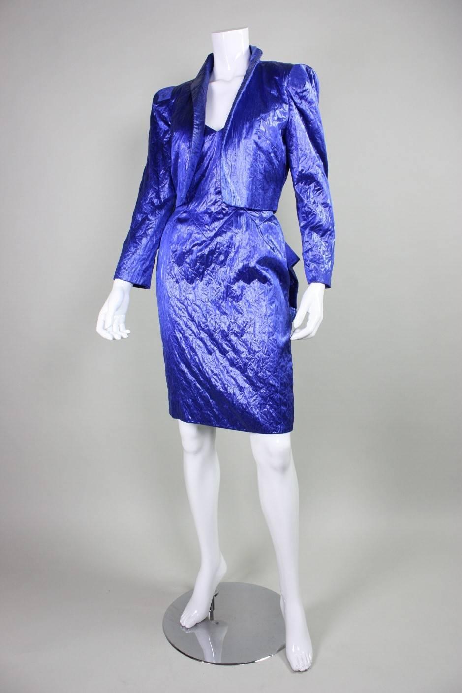 Vintage cocktail dress and jacket from Loris Azzaro is made of textured blue fabric and dates to the 1980's.  The dress has a jagged geometric neckline that is echoed in the waistline of the skirt.  Origami-like folding on the backside of the dress