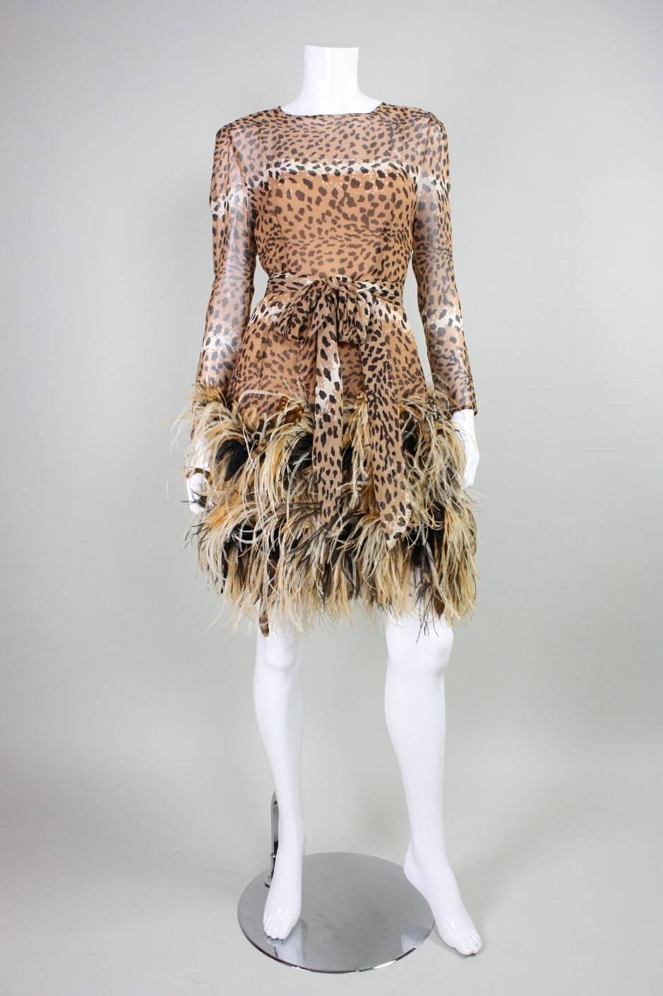 Vintage cocktail dress from Bill Blass dates to 1990 and retailed at Bergdorf Goodman.  It is fashioned out of leopard-printed silk chiffon with a  feathered skirt. Long sleeves have two looped covered button closures at wrists. Dress is lined with