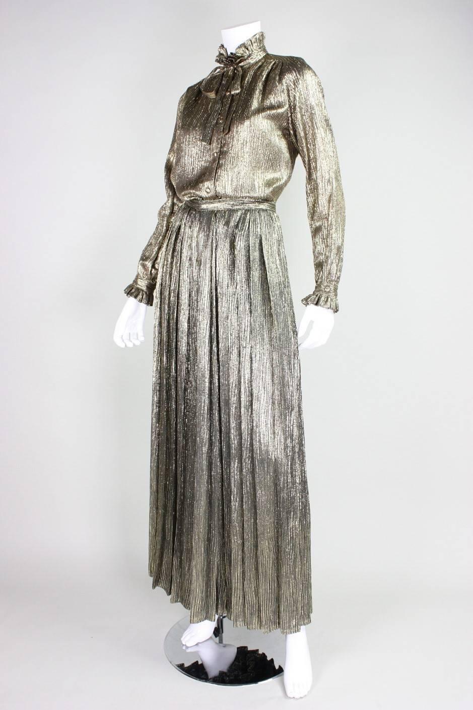 Vintage ensemble from Adolfo dates to the 1970's and is made of metallic gold lame fabric. Long-sleeved blouse has high neck with ruffled collar, center front neck tie, and covered button front closure.  High-waisted palazzo pants have center back