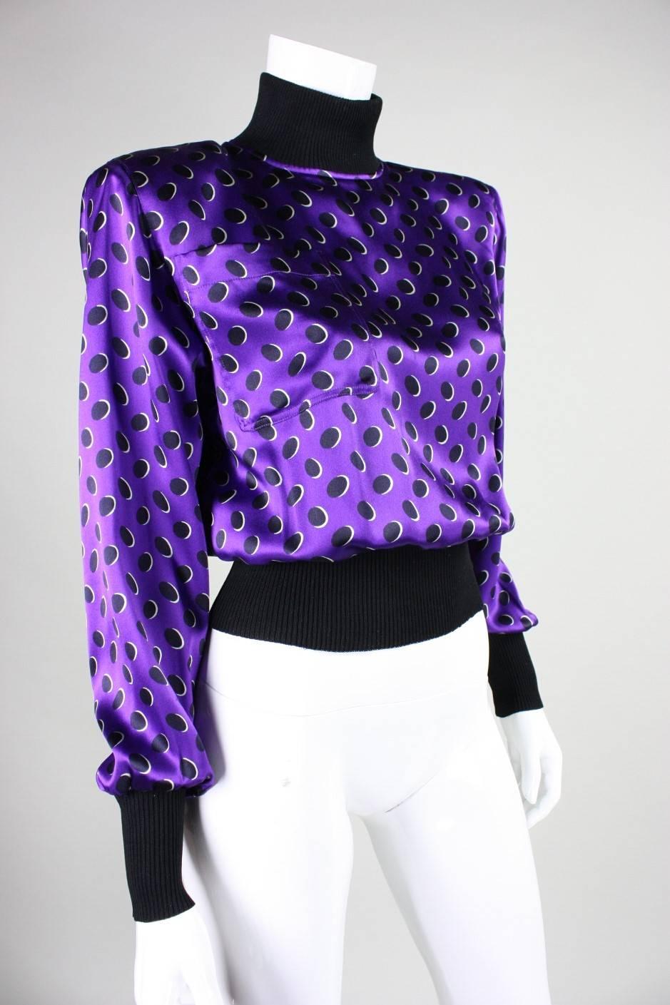 Vintage blouse from Emanuel Ungaro dates to the 1980's and is made of purple silk with a black polkadotted print.  Black ribbed turtleneck, cuffs, and waistband.  Single patch pocket at breast.  Padded shoulders.  Unlined.  Center back