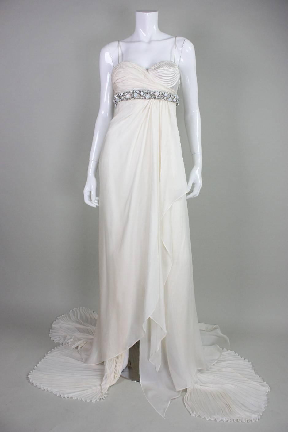 Roberto Cavalli silk chiffon gown likely dates to the 1990’ and is made of ivory silk chiffon with a rhinestone encrusted band under bust. One breast has gathered chiffon while the other is “exposed” with quilted detailing. Fabric is gathered under