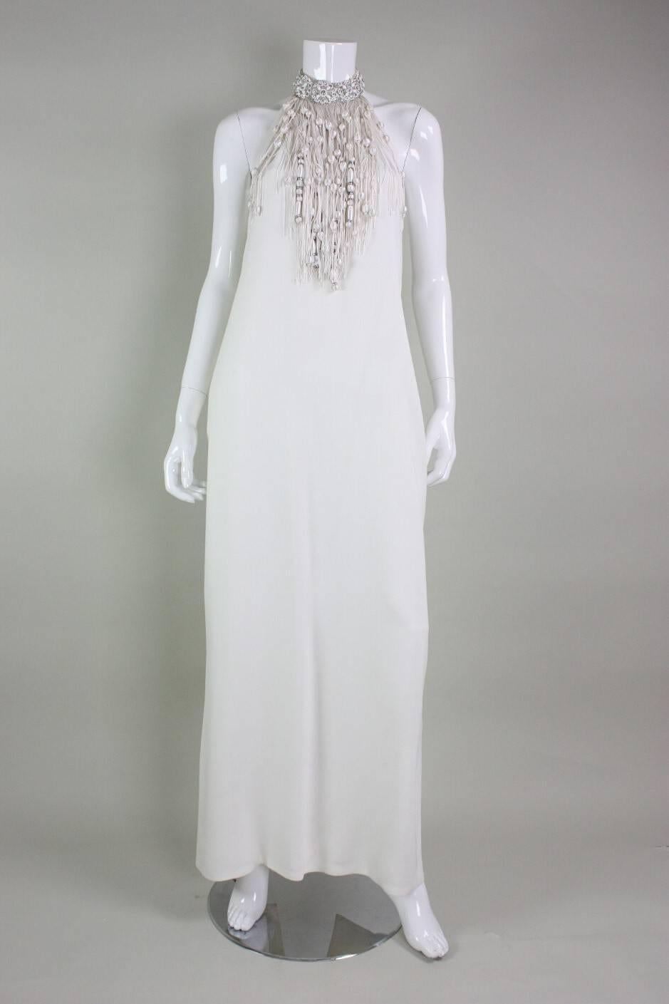 Vintage Valentino column gown is made of off-white crepe with fringed neckline.   Mock neck is encrusted with beading of various sizes and rhinestones.  Halter style with upper and mid-back exposed.   Center back slit in skirt.  Fully lined.  Center