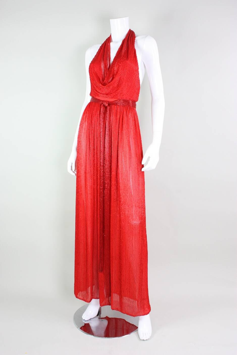 Vintage gown from Halston dates to the 1970s and retailed at Sara Fredericks.  It is made of fire engine red chiffon with red bugle beads throughout.  Halter with cowl neck and open back.  Detached belt is fully beaded on one side.  Lined with red