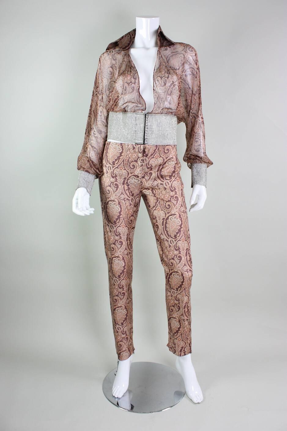 Vintage ensemble from Dolce & Gabbana likely dates to the 1990’s.  Blouse is made of a lightweight paisley silk chiffon with wide rhinestone bands at the waist and cuffs.  Flat front silk pants have patch pockets on the buttocks.  Zippered ankle