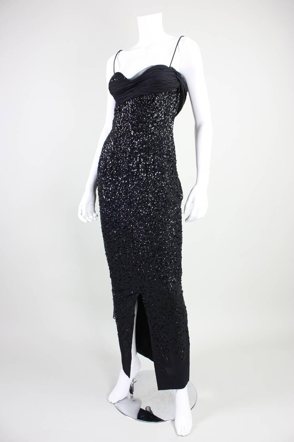 Vintage gown from Frank Starr likely dates to the late 1950’s to early 1960’s and is made of black crepe with black sequins sewn in a squiggle pattern that diminishes in density from top to bottom.  Gathered black chiffon band starts at right
