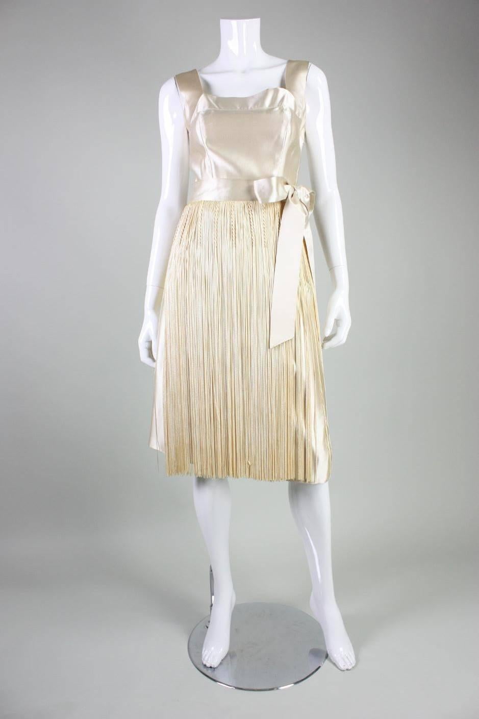 Vintage party dress from Ben Reig dates to the 1950's and is made of cream-colored silk satin.  Fitted bust features a squared neckline and wide straps.  Knee-length skirt is fully covered with fringe. Waistband ties at side waist. Unlined. Side