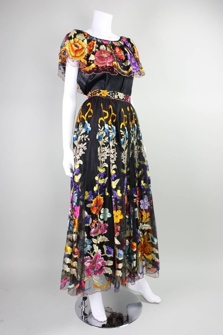 Vintage wedding ensemble from Mexico likely dates to the mid 20th century.  It is made of black net over a synthetic black fabric and features brightly colored floral hand embroidery throughout the full skirt and the ruffle of the neckline. Blouse