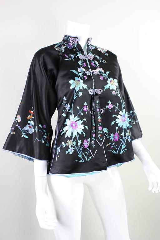 Vintage 1930's jacket is of Chinese origin and is made of black silk and features hand embroidery that depicts flowers, birds, and butterflies in a cool color palette.  Five center front frog closures.  Vents at center back and both side seams. 