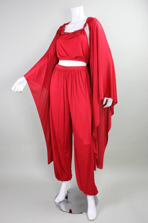 Vintage Holly's Harp three piece ensemble dates to the 1970's and is made of a cherry red matte jersey.  Sleeveless cropped top with braided gold bullion trim and center back hook and eye closures. Harem pants have elasticized waist and cuffs with