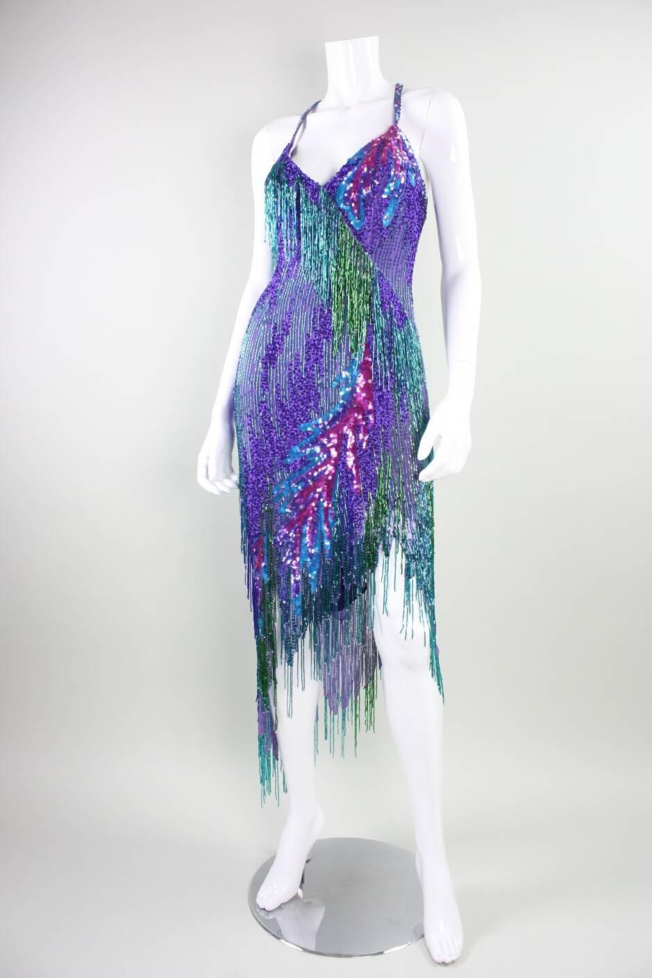 Spectacular cocktail dress from Bob Mackie dates to the 1980's and retailed at Amen Wardy.  It is made of purple silk that is covered in jewel-toned bugle beads that are sewn directly on to the fabric as well as ones that dangle down in dense rows