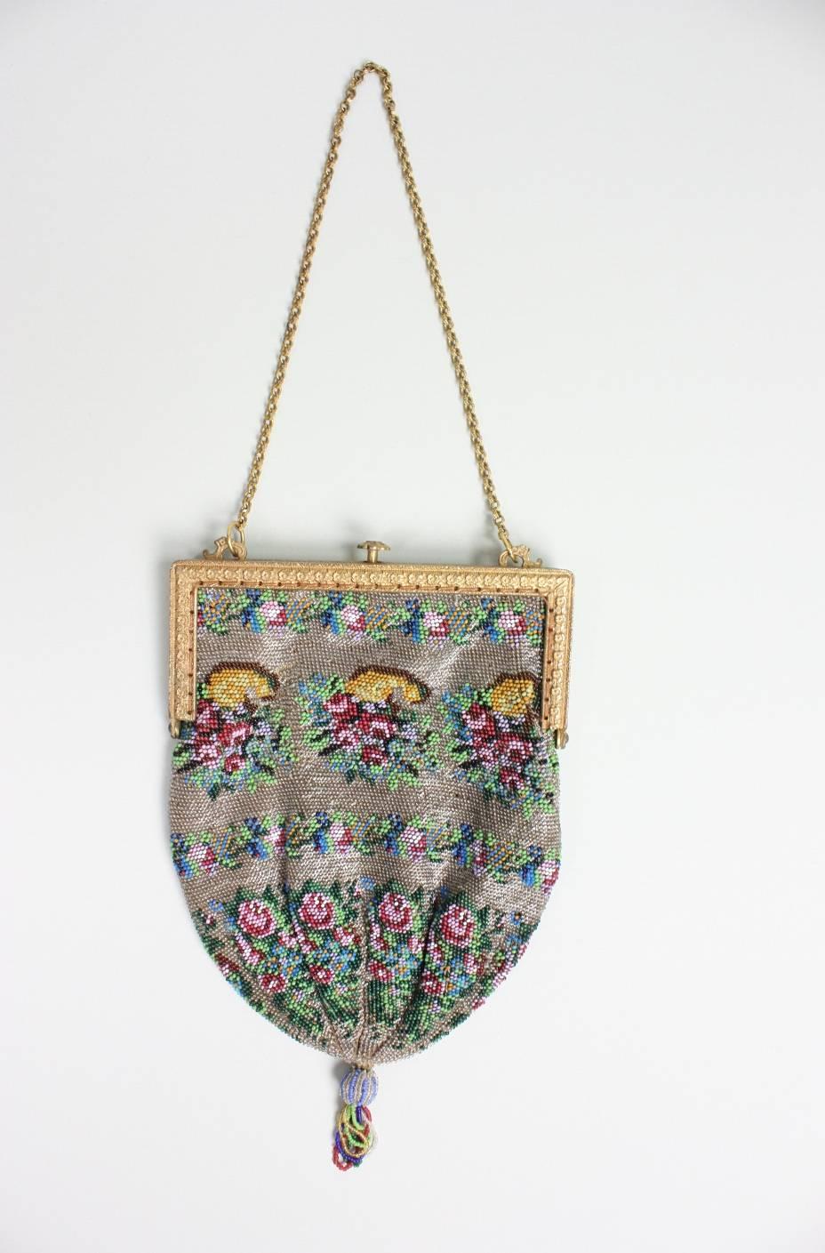 Vintage handbag dates to the 1920's and is comprised entirely of small seed beads.  Floral motif is worked in red, pink, and varied shades of blue.  Gold-toned frame is set with red and green rhinestones.  Push clasp.  Chain strap.  Red silk