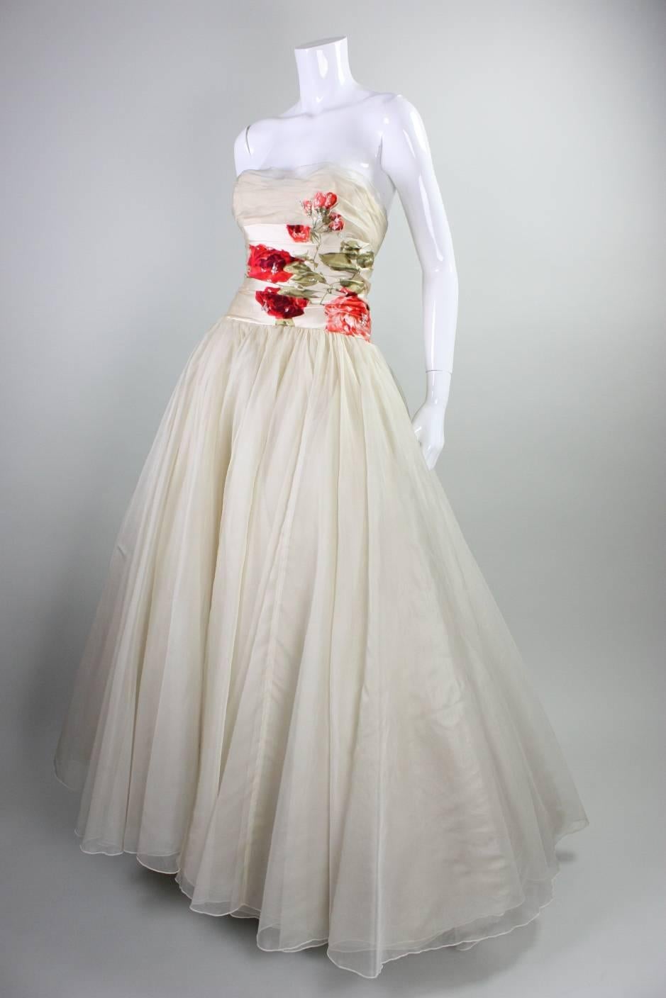 Vintage anonymous ball gown dates to the 1950's and is made of multiple layers of cream silk organza.  Silk satin waistband and skirt panels feature striking red cut velvet flowers with beaded detailing.  Fitted bodice is strapless and features
