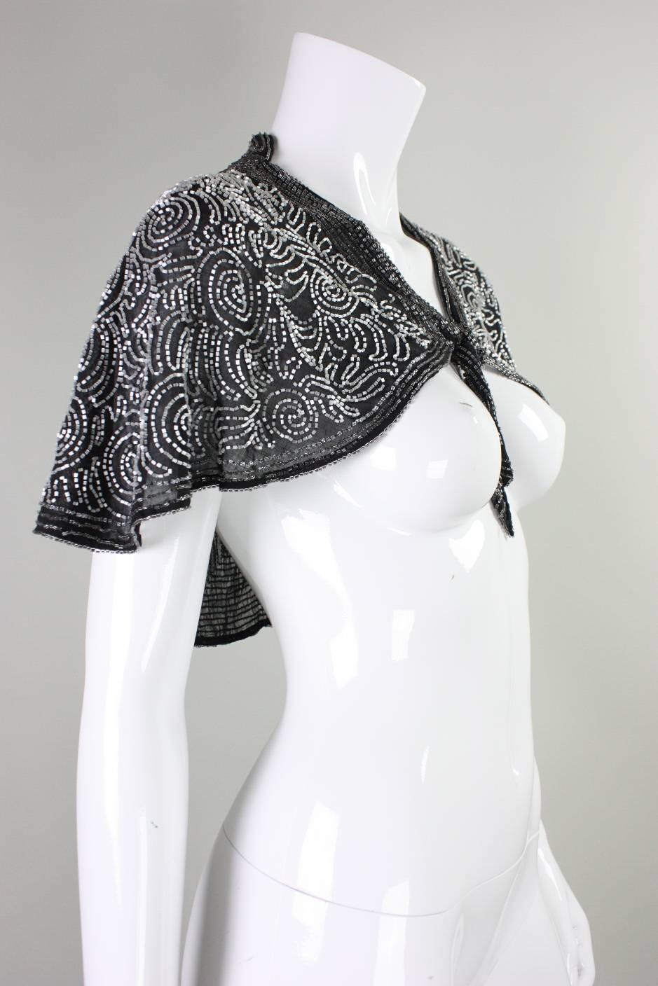 Vintage capelet dates to the 1930's and is made of lightweight black cotton that is covered in an allover pattern with glass bugle beads.  Tag at center back neckline reads 