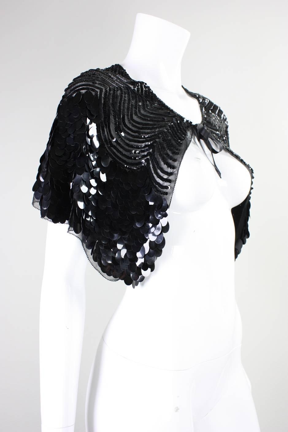 Vintage capelet dates to the 1930's and is made of sheer black cotton that is covered in scalloped rows of black sequins and paillettes.  Center front ribbon tie closure.  Unlined.