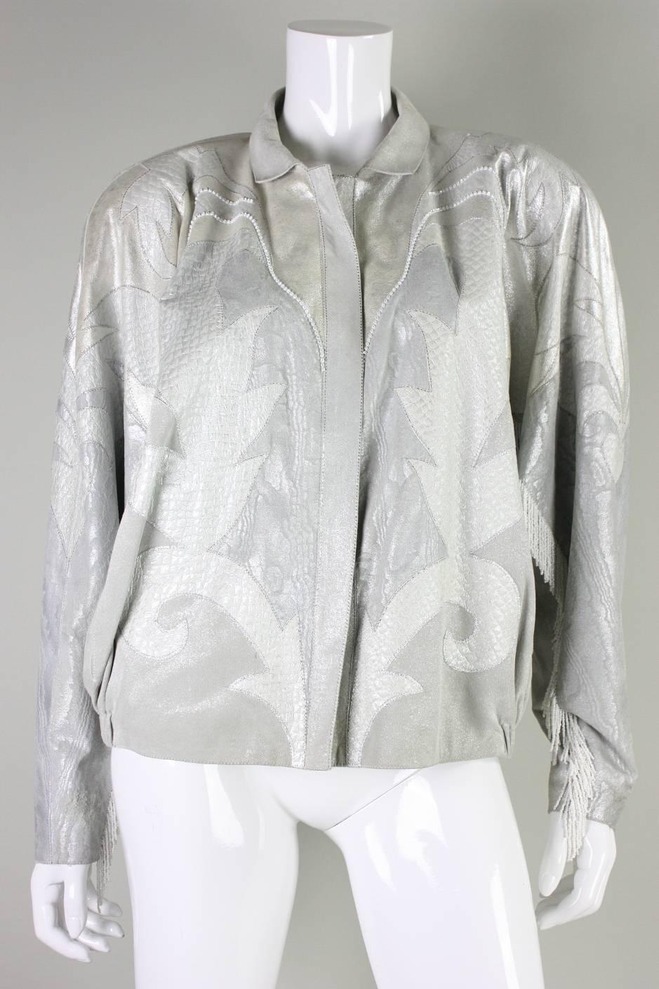 Vintage jacket from Roberto Cavalli is made of metallic silver suede with fabrics and other skins appliqued on.  Jacket features white beaded fringe down the backs of the sleeves.  It has a turn-down collar, rhinestone detailing, and side seam