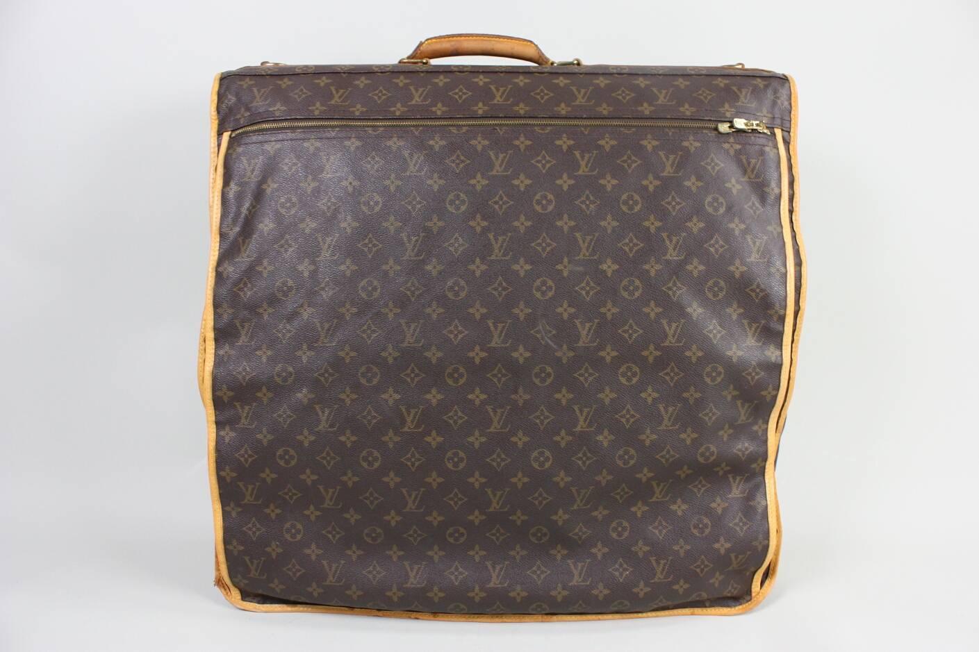 Vintage unisex Louis Vuitton garment carrier is made of brown and tan monogram coated canvas and dates to the 1990's.  It has brass hardware, tan vachetta leather trim, single rolled top handle and single exterior pocket with zip closure. Single