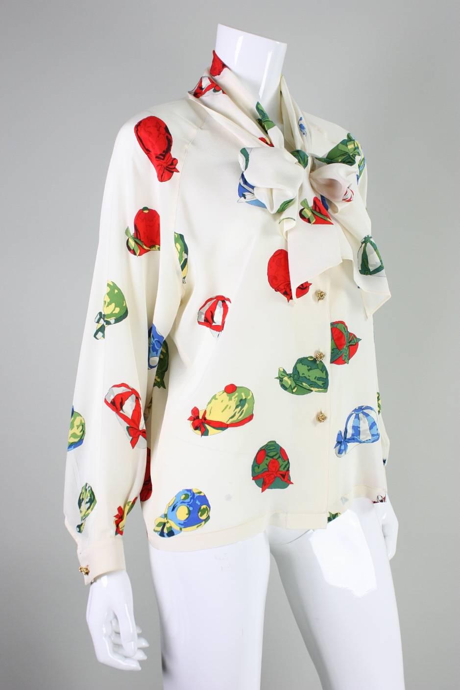 Vintage blouse from Hermes is made of cream silk with a jockey cap print.  It features a sash that is attached at the center back neck that can be tied in a variety of ways.  Scoop neck.  Long sleeves with buttoned closure.  Center front gold-toned