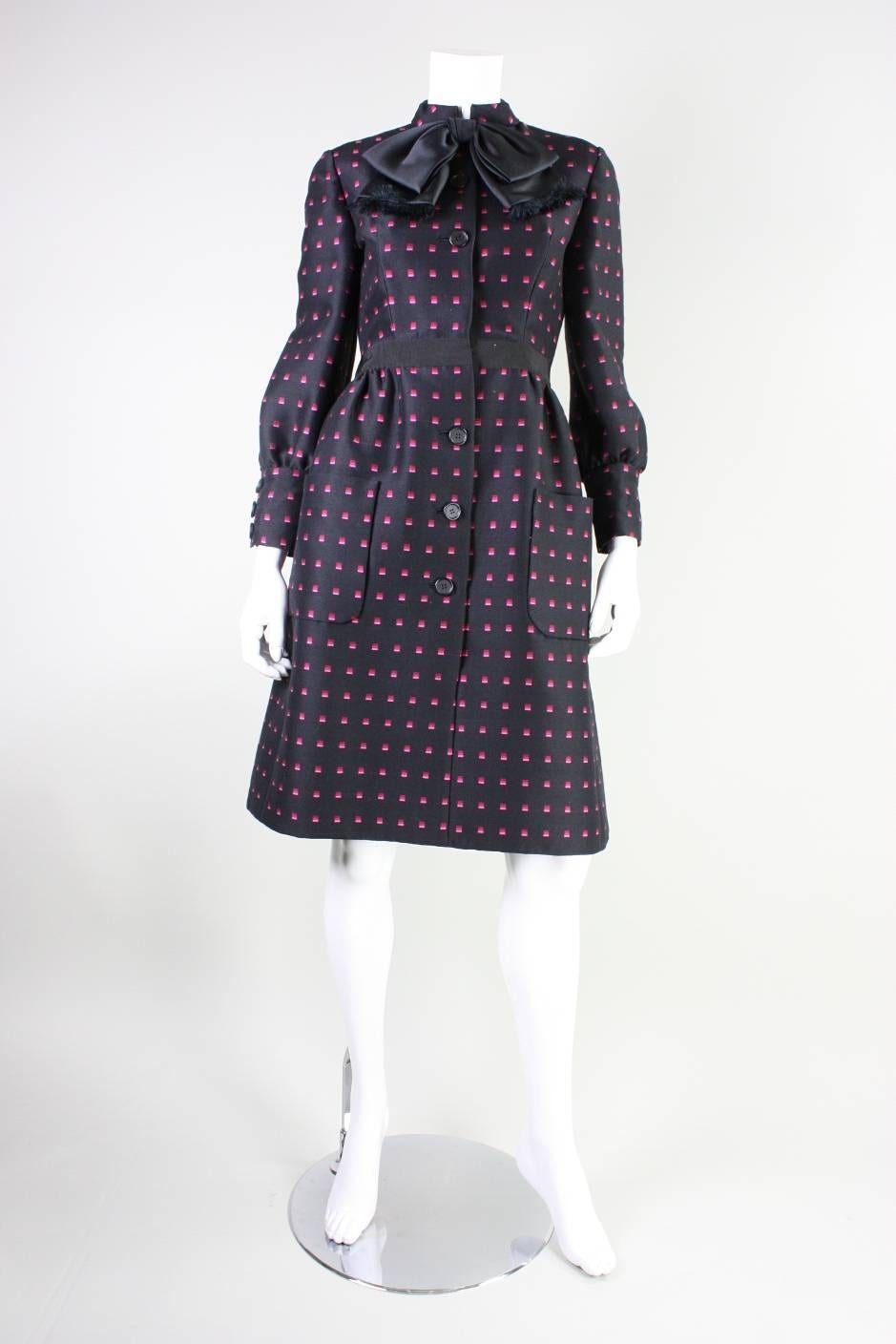 Vintage cocktail or day dress from Chester Weinberg dates to the 1960's and is made of a black wool blend fabric that has a geometric pattern in three shades of pink.  High neckline has a large center front bow.  Patch pockets at front hips.  Long