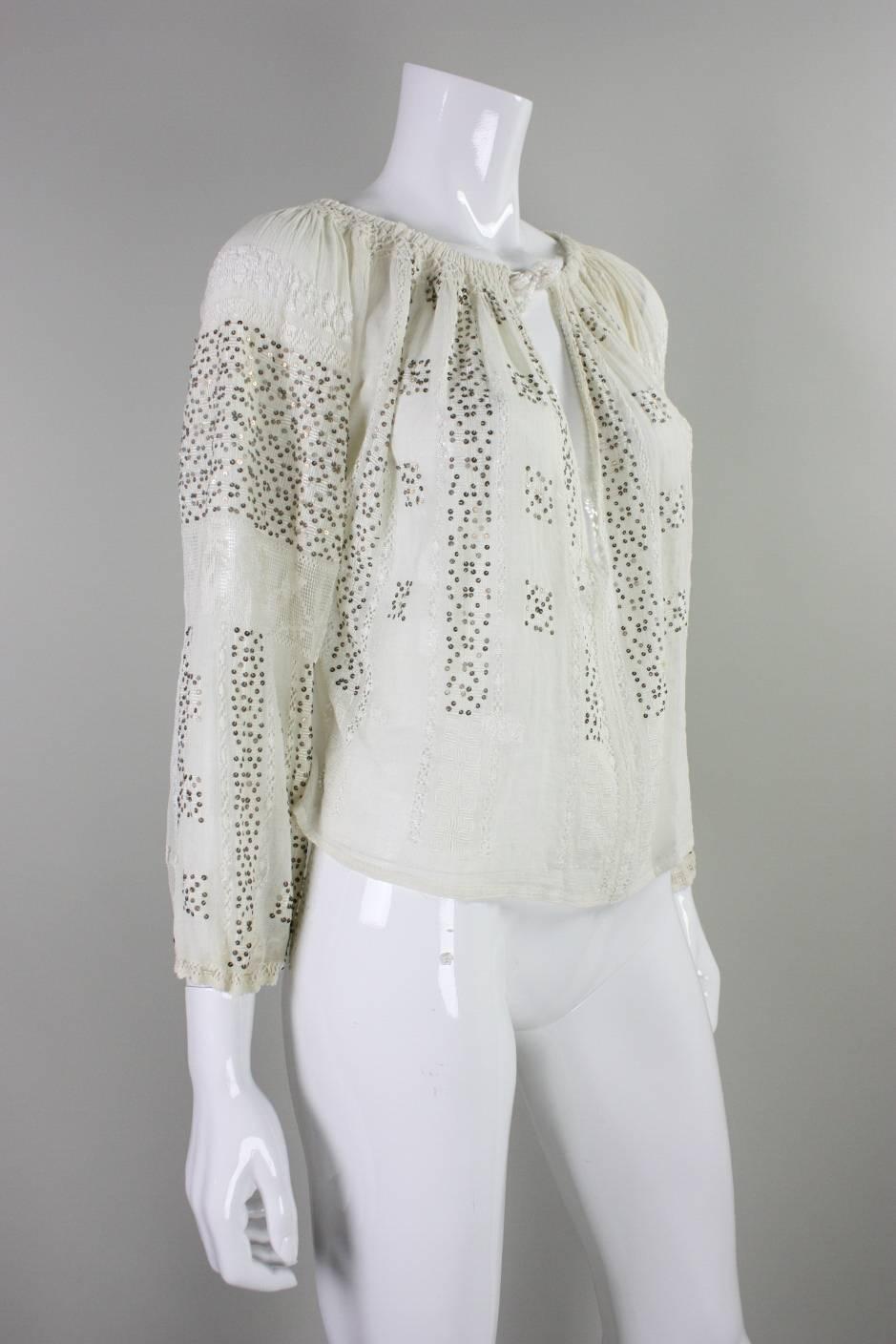 Vintage Eastern European blouse dates to the 1930's and is made of cream colored cotton gauze with openwork and metallic sequins. It features a keyhole neckline with a center front neck drawstring tie.  Long sleeves with drawstring cuffs. 