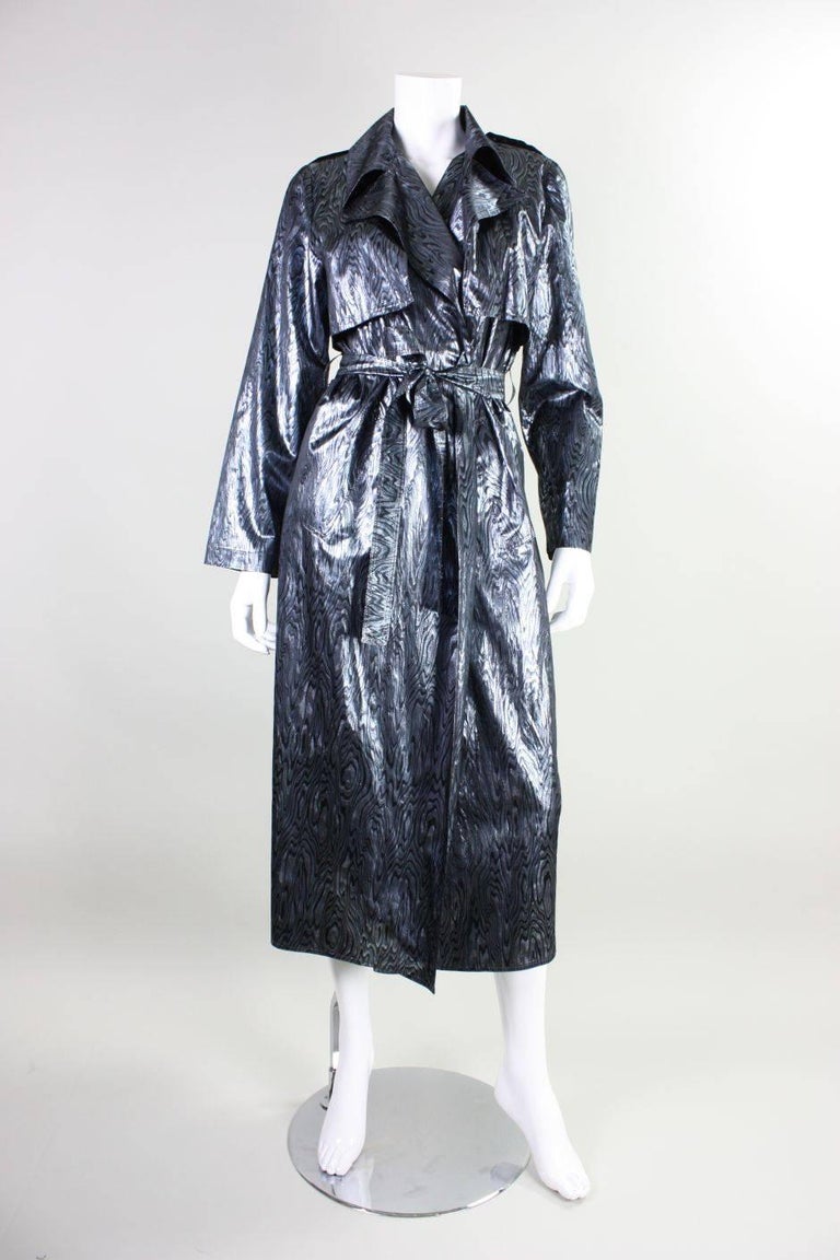 Vintage trench coat by Vicky Tiel retailed at Bergdorf Goodman and dates to the 1980's through 1990's.  It is made of silver and black lame fabric with a woodgrain pattern.  Slanted pockets at hip. Center back vent. Unlined. No closures outside of a