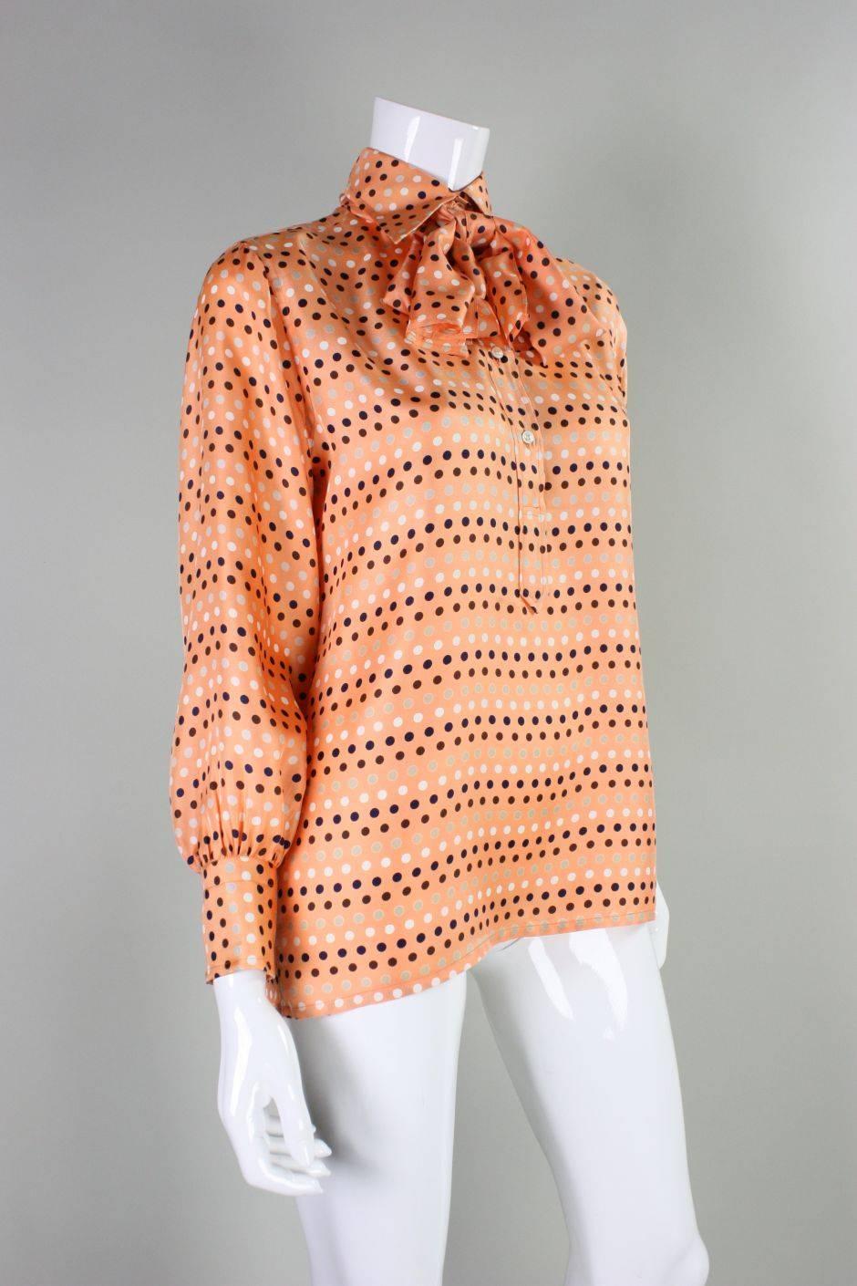 Vintage blouse from Valentino dates to the 1970's and retailed at I. Magnin.  It is made of melon-colored silk with polka-dots.  Detached sash can be worn around the neck, at the waist, in the hair or not at all.  Turn down collar with double button