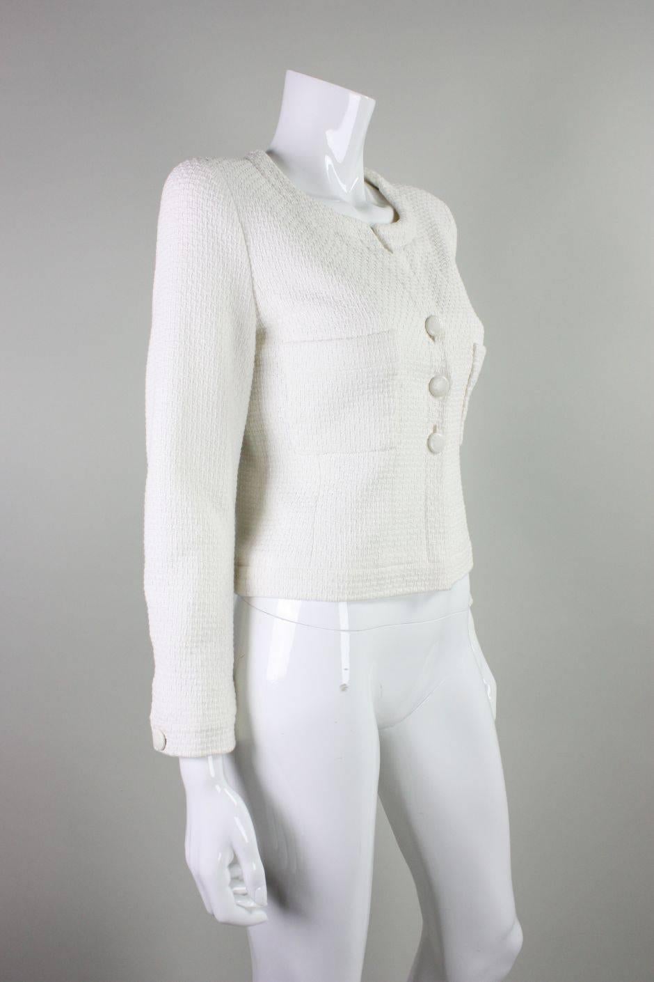 Vintage cropped jacket from Chanel dates to 1998 and is made of  white textured cotton.  Two patch breast pockets.  Three center front button closures.  Long sleeves with single buttoned cuffs.  Interior gold chain at waist.  
Labeled a size
