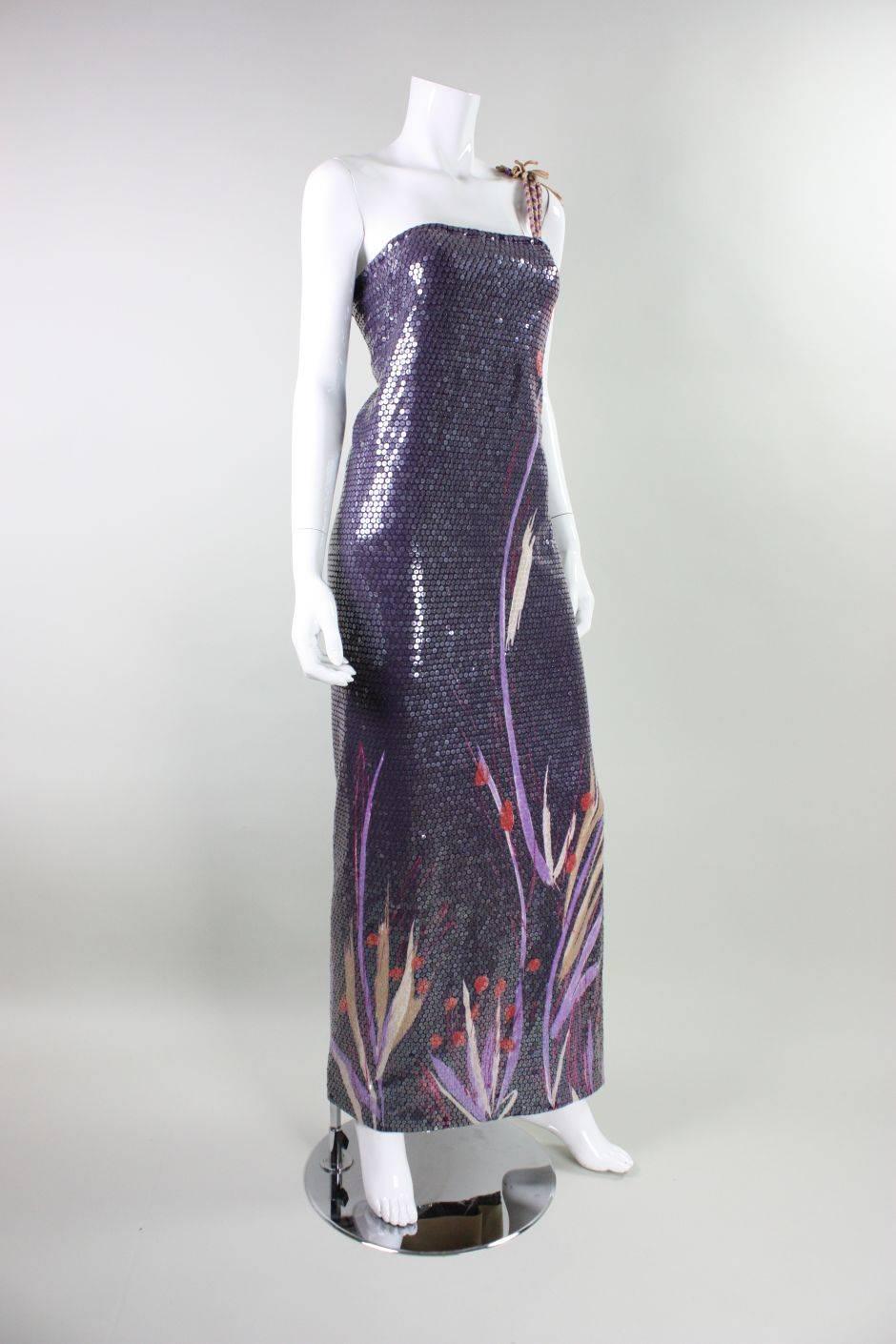 Vintage anonymous gown dates to the 1970's and is made of purple stretch fabric with a floral border print that comes up from hem. Three multicolored braided shoulder straps on left shoulder. Side back slit in skirt. Fully lined with a stretchy nude