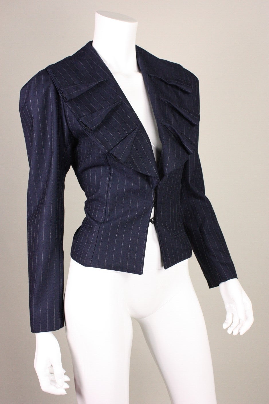 Vintage blazer from Norma Kamali's OMO line is made of a fine navy wool with a pinstripe pattern.  Wide shawl collar with raised detailing.  Center front large hook and eye closures.  Lined.

No size label, but we estimate it would fit a size