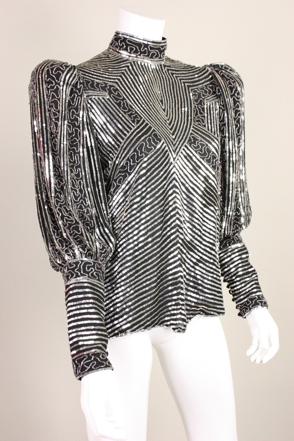 Vintage blouse is made of black silk and covered in silver sequins and bugle beads.  Mock neck.  Exaggerated shoulders created with shoulder pads.  Sleeves button up the forearm with looped closure.  Center back same closure.
Lined.

Labeled size